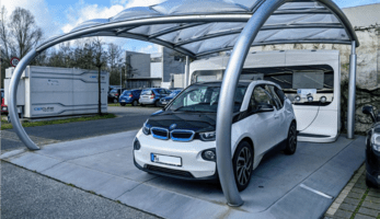 EV charging station on company-ground, with PV cells on roof and stationary energy storage in the background.