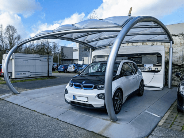 EV charging station on company-ground, with PV cells on roof and stationary energy storage in the background.