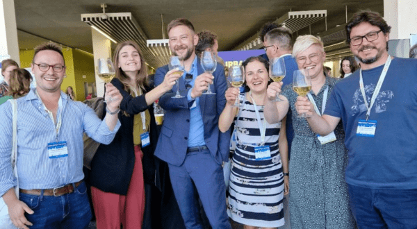 Six people holding up glasses of white wine, toasting toward the camera