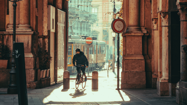 Man cycling through an arch in Milan, with the sun rising in the background.