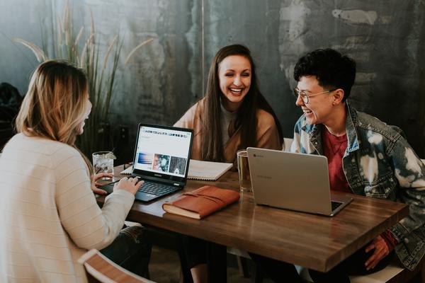 Three young people sitting in front of their laptops at a table laughing.