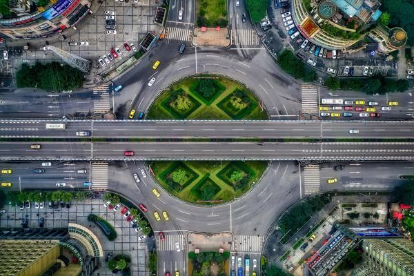 Aerial view of a very large intersection with many lanes of cars, pedestrians, and green space around the roads.