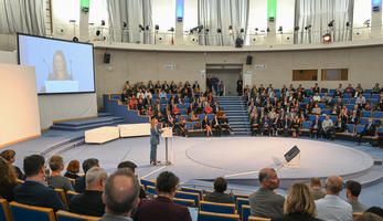 Auditorium of audience members watch a speaker on stage during the opening plenary of Urban Mobility Days 2022.
