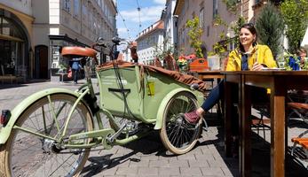 Woman sitting at an outdoor cafe with her bicycle beside her. 