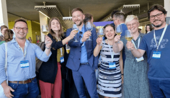 Six people holding up glasses of white wine, toasting toward the camera