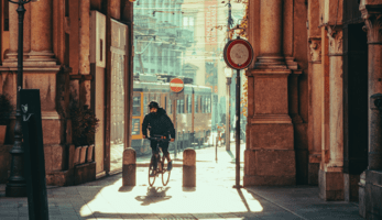 Man cycling through an arch in Milan, with the sun rising in the background.