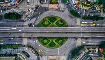 Aerial view of a very large intersection with many lanes of cars, pedestrians, and green space around the roads.
