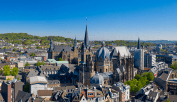 Picture of Aachen's city centre, including its cathedral, with green hills in the background.